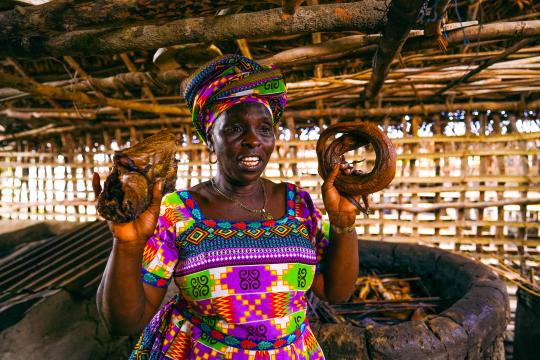 Yata, one of the women fish mongers from Sierra Leone who started using solar refrigerators. Photo : UNDP/Mohamed Kanu A fishmonger from Sierra Leone smiling and showing dried fishes in her local shop.
