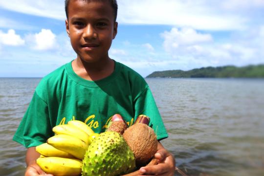 Young boy from Federated States of Micronesia (FSM) poses for a photo holding a bowl of fresh fruit.