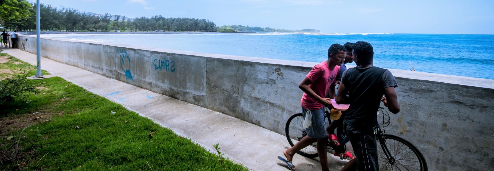  Jóvenes caminando en la playa a lo largo de la pared costera que proporciona protección contra marejadas ciclónicas en Riviere des Galets, en el sur de Mauricio