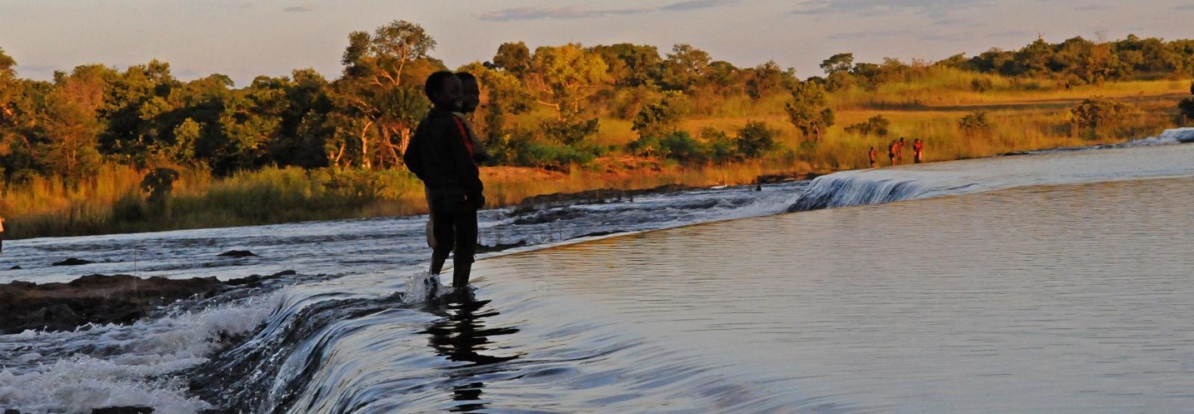 Un enfant se tient debout dans une rivière au crépuscule